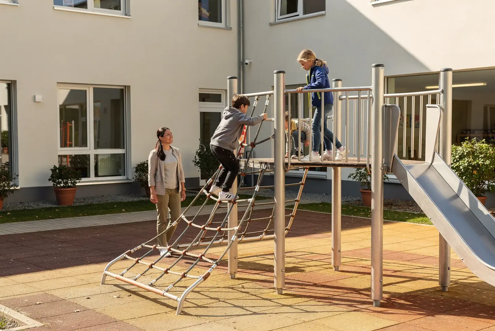 Vier Jugendliche stehen lachend an den Stangen eines übergroßen Menschenkickers im Freien, helles Tageslicht, sommerlicher Hof einer Jugendeinrichtung, Bewegung eingefangen.